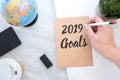 Hand holding pen writing 2019 Goals on brown paper with blue globe,blackboard,coffee cup on marble table.new yearÃ¢â¬â¢s resolutions